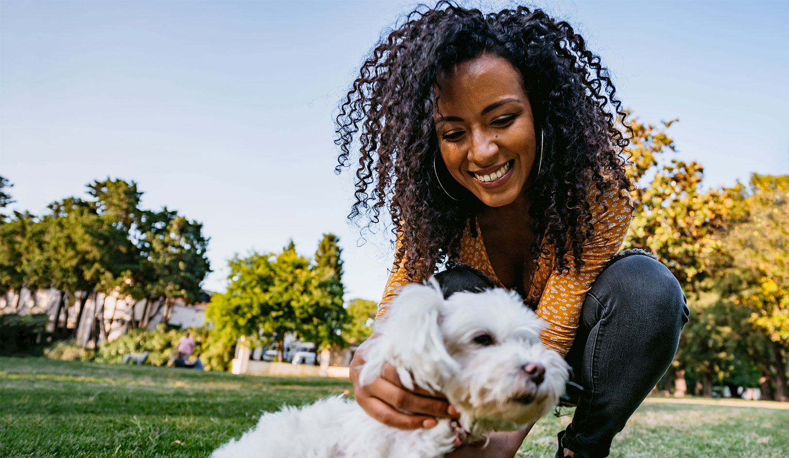 Woman kneeling in park petting small white dog